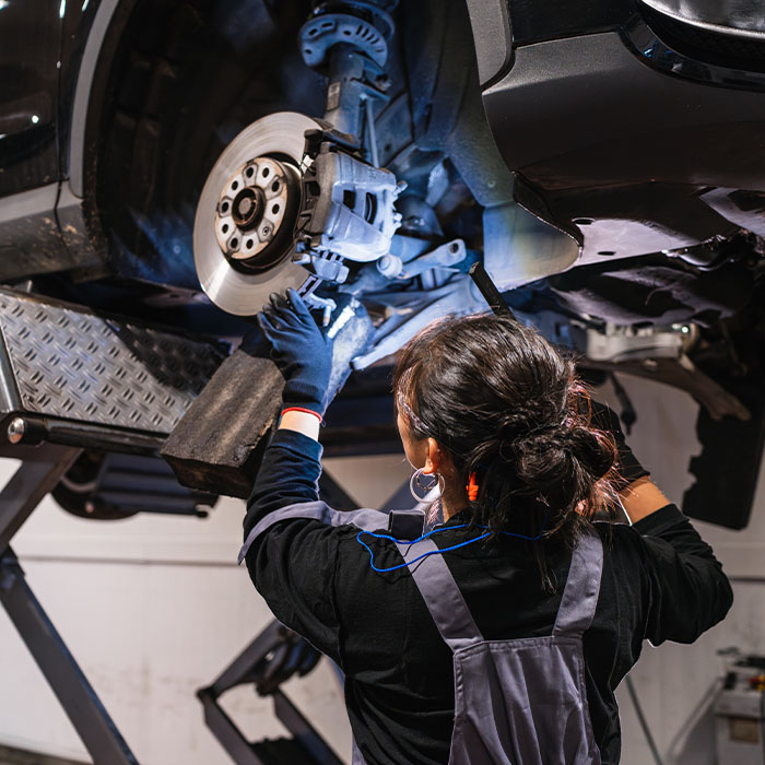 Female mechanic inspecting car brakes on hydraulic lift in repair shop
