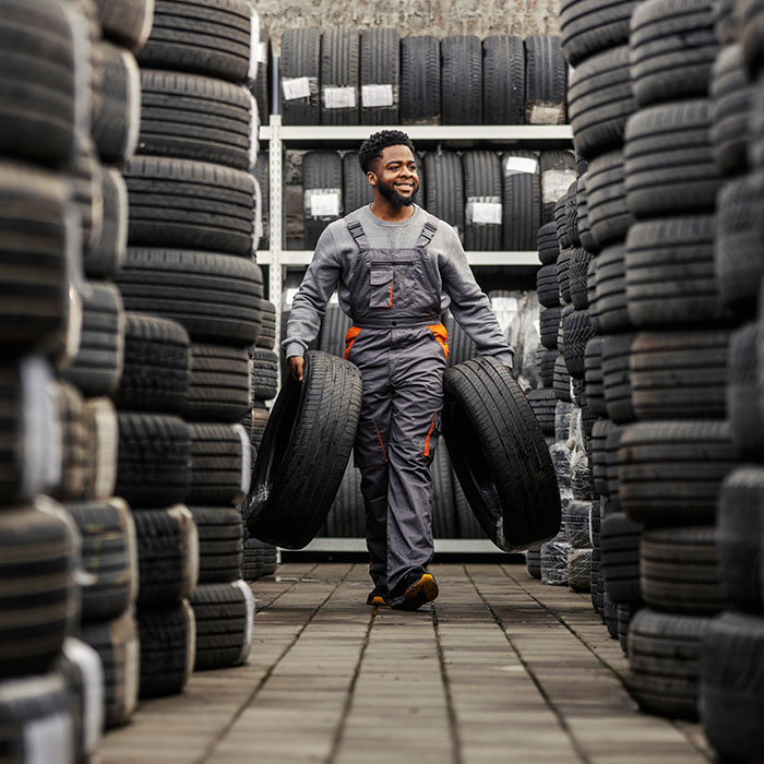 Smiling technician carrying car tires at car service