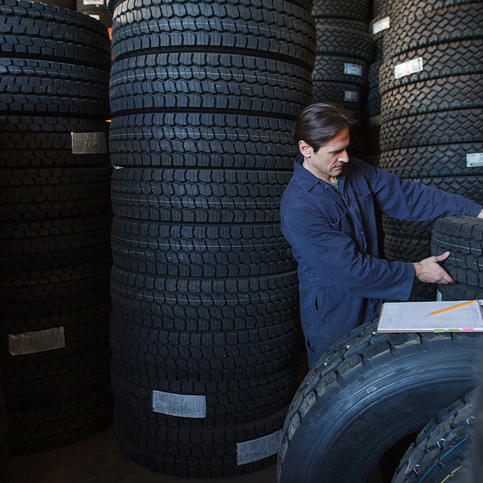 Mechanic lifting new car tire from stack of tires inventory