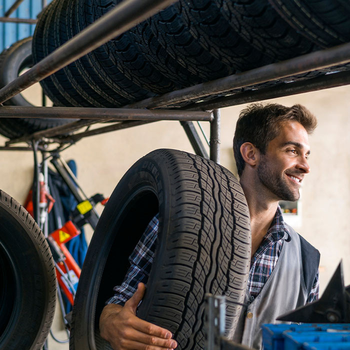 Smiling mechanic carrying tire at auto repair shop